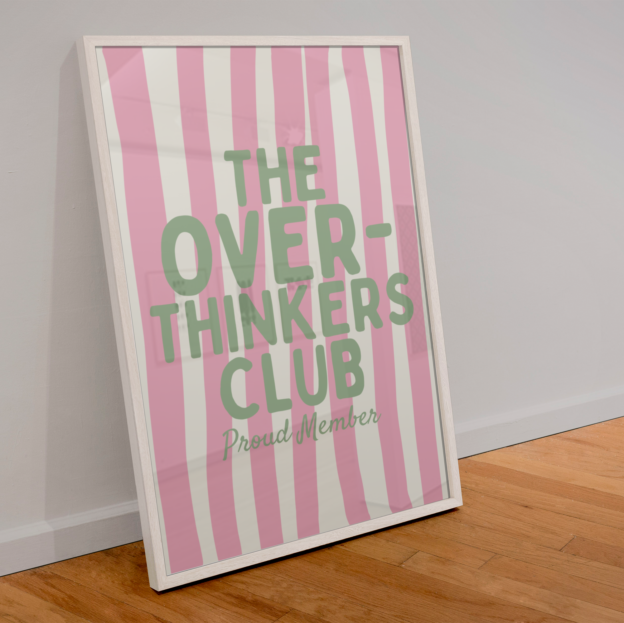 Framed poster with 'The Over-Thinkers Club' text on a pink and white striped background, leaning against a wall.