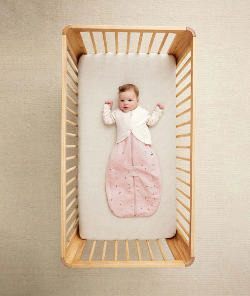 Baby lying in a wooden crib with a pink sleeping bag on a beige background - shop Boutiquey home st Neots Cambridgeshire 