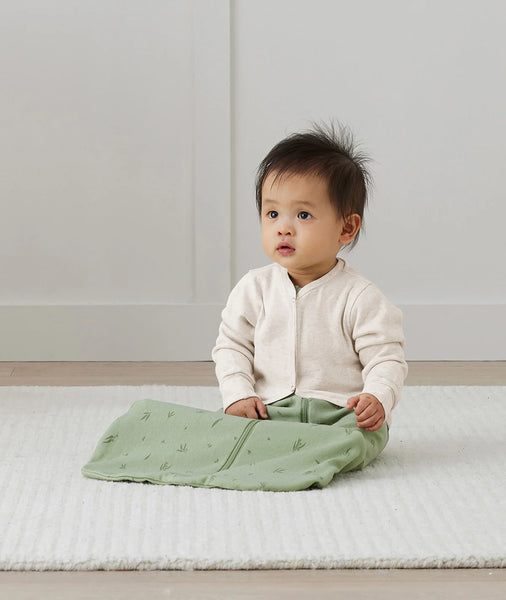 ergoPouch arm warmers - Baby sitting on a white rug with a green swaddle blanket